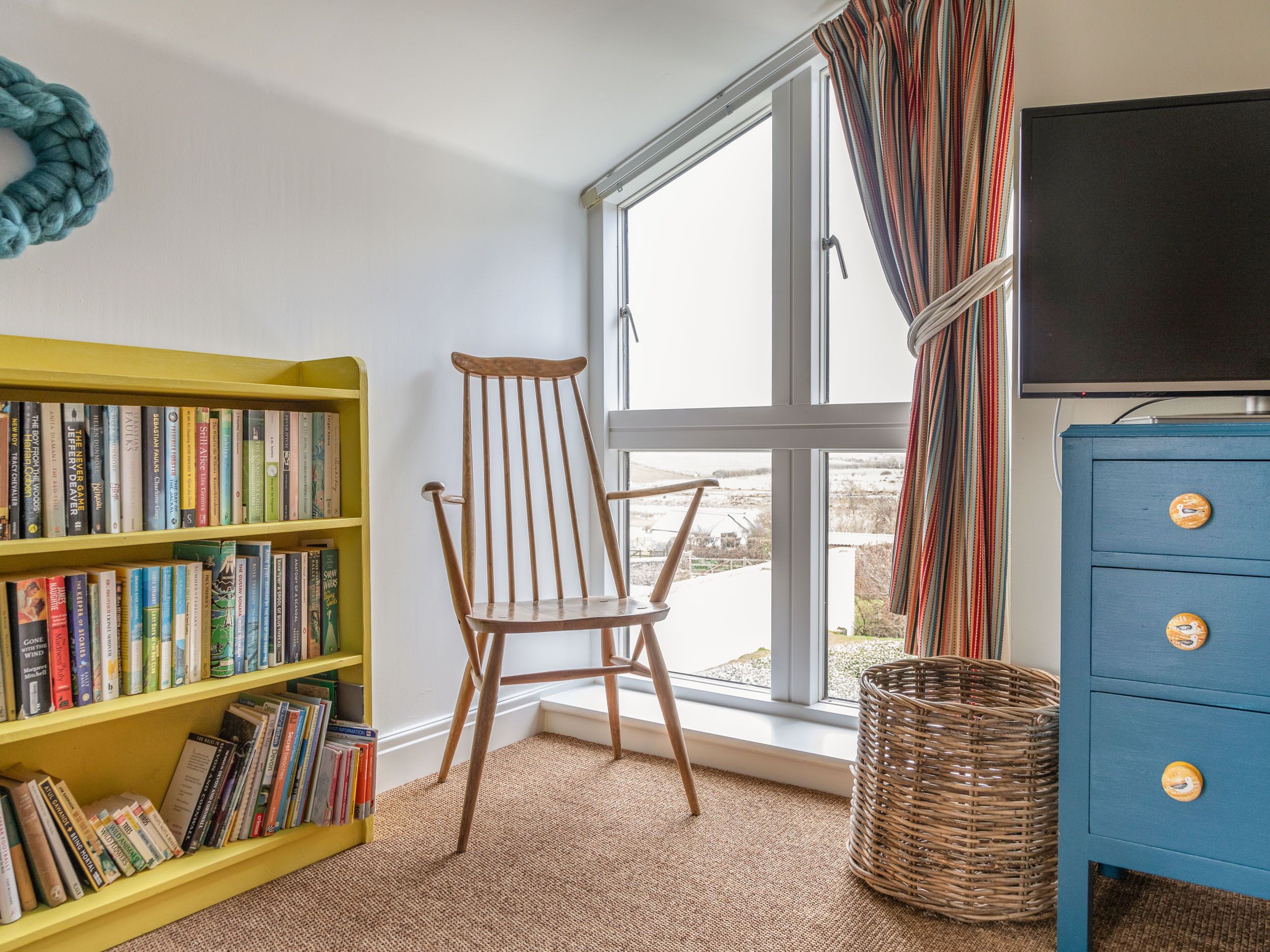 Una habitación con estantería, una silla de madera, televisión y una ventana con cortinas.