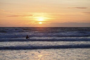 Een zonsondergang boven de oceaan met golven en een silhouet van een persoon in het water.