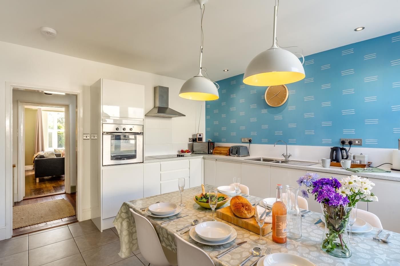 A modern kitchen with white cabinets, a built-in oven, a microwave, and a blue backsplash.