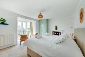 A bedroom with a large bed, a window, a chair, a fireplace, and a plant.