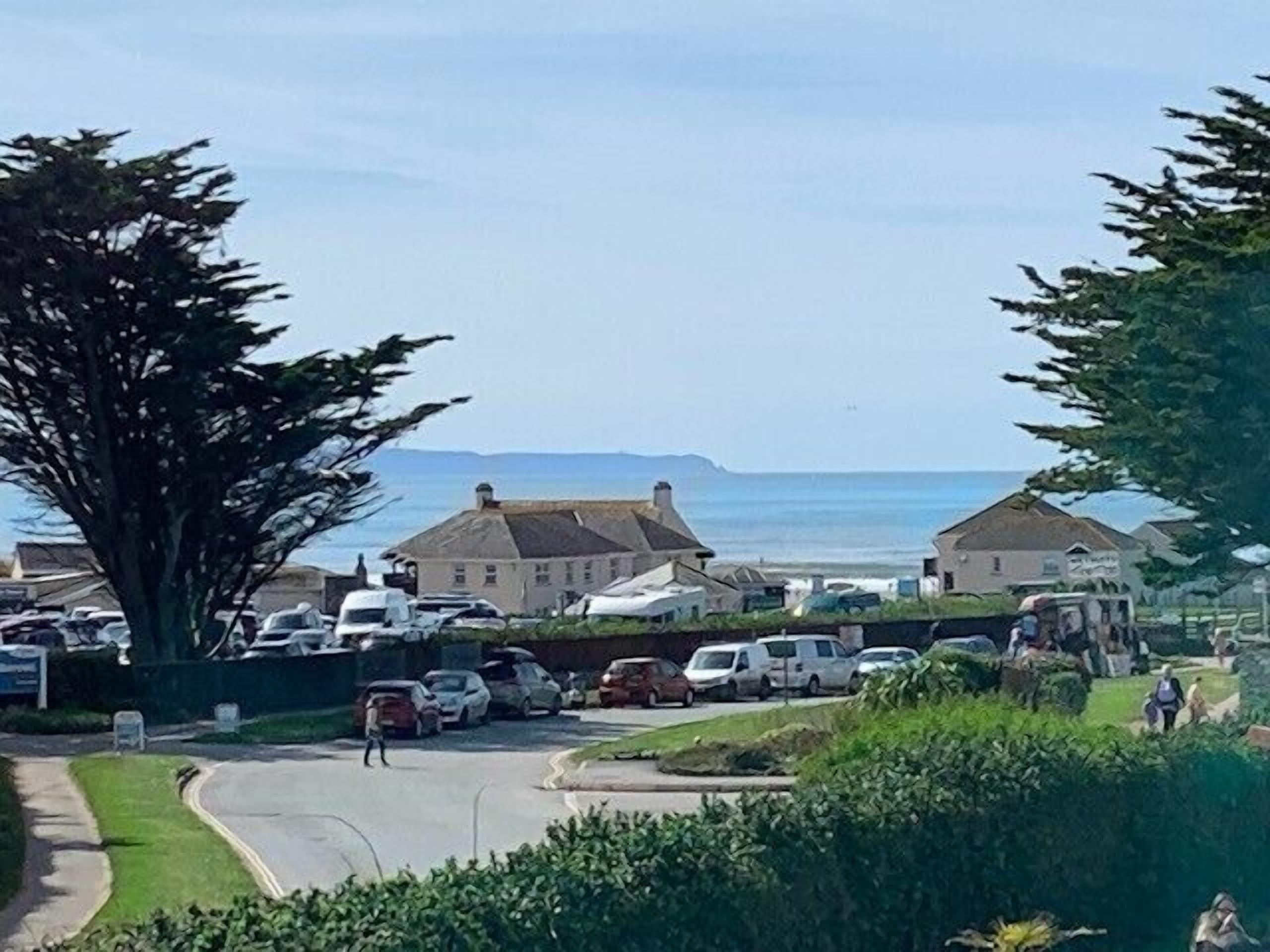 A coastal residential area with houses, parked cars, and a road leading to the sea.
