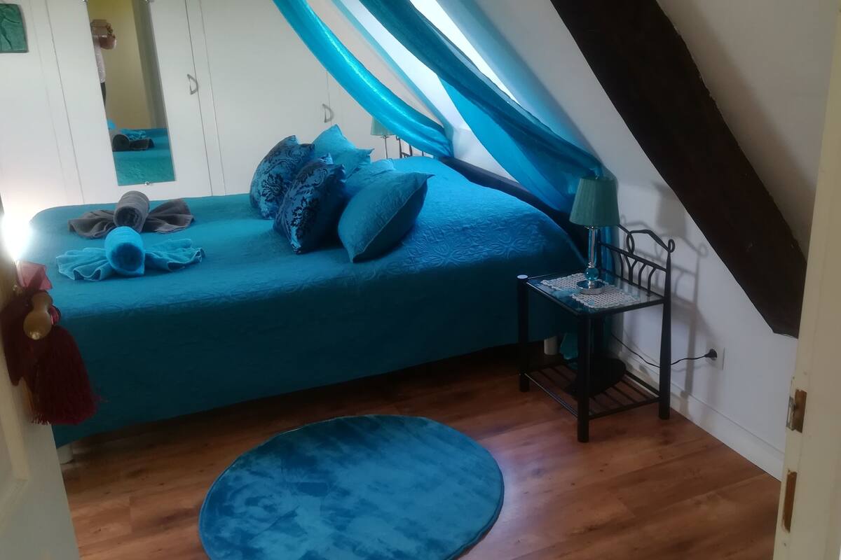 A small, cozy room with a bed, a side table, and a blue rug.