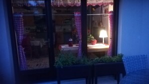 Una habitación con una mesa, sillas, una lámpara y un ventanal con cortinas a cuadros.