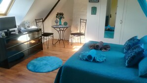 Una habitación acogedora con una cama, un escritorio, una silla y una pequeña mesa con un jarrón de flores.