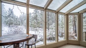 Kulmassa sijaitseva huone, jossa on suuri ikkuna, josta avautuu näkymä lumiseen metsään.