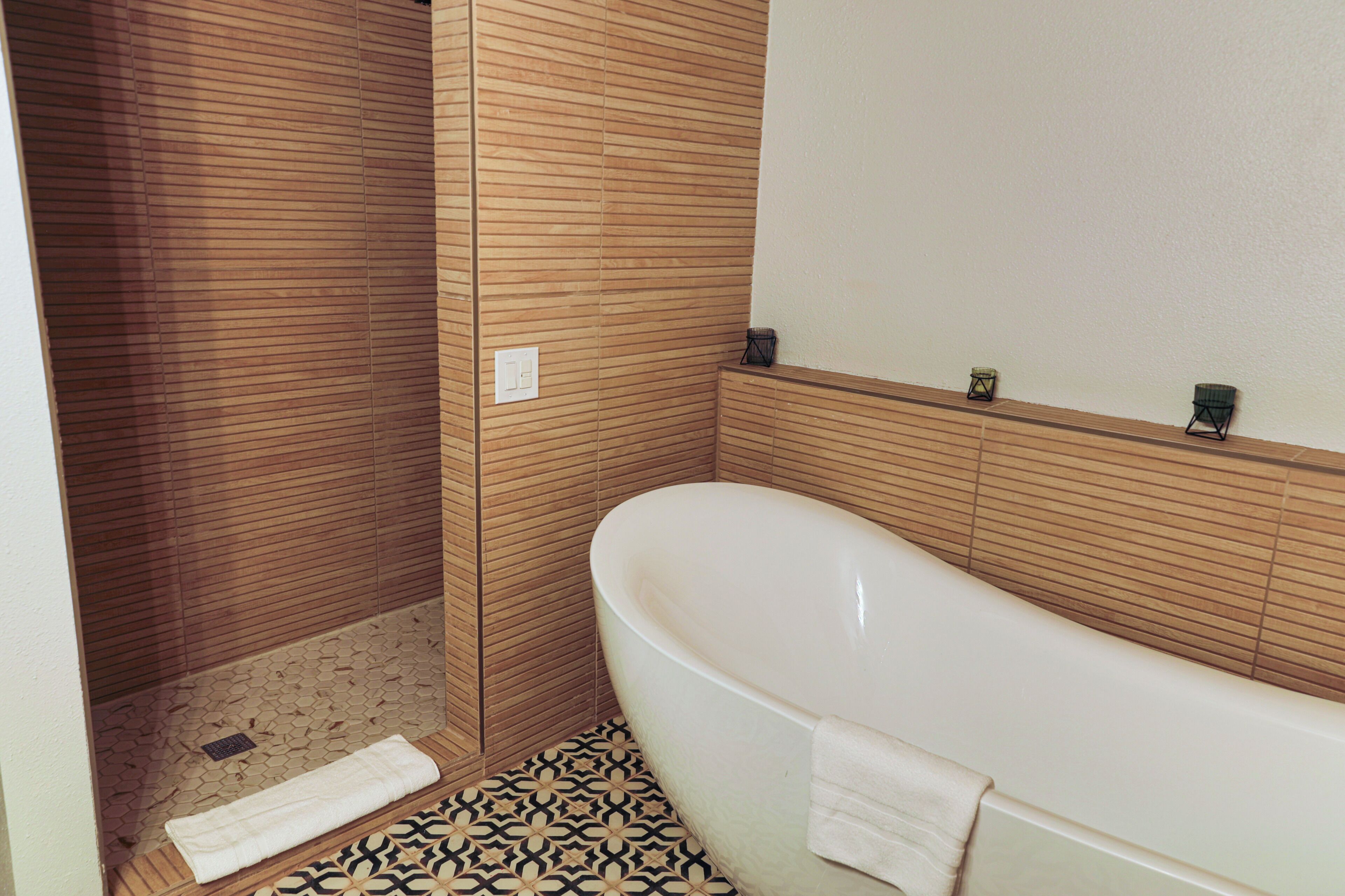 Une salle de bain avec une baignoire sur pieds, un espace douche, des carreaux de sol à motifs et un panneau mural en bois.