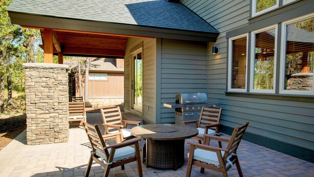 An outdoor patio with a round table and four chairs, a stone pillar, and a barbecue grill. - Caldera Escape with Access to Forest House (Sunriver)