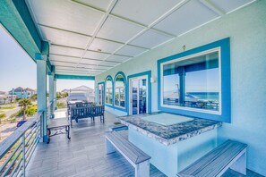 Ein überdachter Außenbereich mit Sitzgelegenheit, einem kleinen Tisch und Blick auf den Strand.