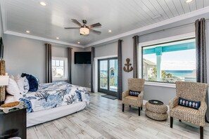 Ein Schlafzimmer mit einem Bett, zwei Korbstühlen und einem Deckenventilator, mit Blick auf den Ozean.