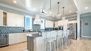 Una cocina moderna con gabinetes blancos, una isla de mármol y taburetes de bar.