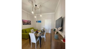 A dining area with a wooden table, white chairs, and a green sofa. There is a painting on the wall and a vase with flowers on the table. - Luxury Apartament's Celso (Palermo)