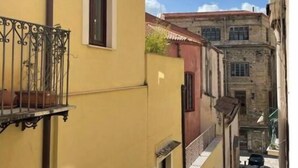 A narrow street with yellow buildings, a balcony with a metal railing, and a clear blue sky. - Luxury Apartament's Celso (Palermo)