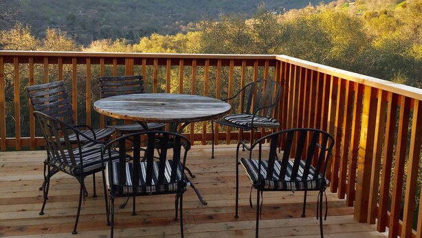 Une terrasse en bois avec une table ronde et quatre chaises, offrant une vue sur un paysage montagneux.