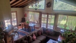 Un vaste espace de vie comprenant une table à manger en bois, des sièges confortables et de grandes fenêtres offrant une vue sur l’extérieur.