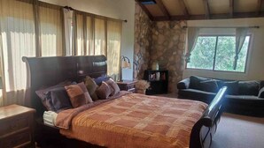 Une chambre avec un grand lit, un mur en pierre, une fenêtre avec des rideaux, une table de chevet, une lampe et un canapé.