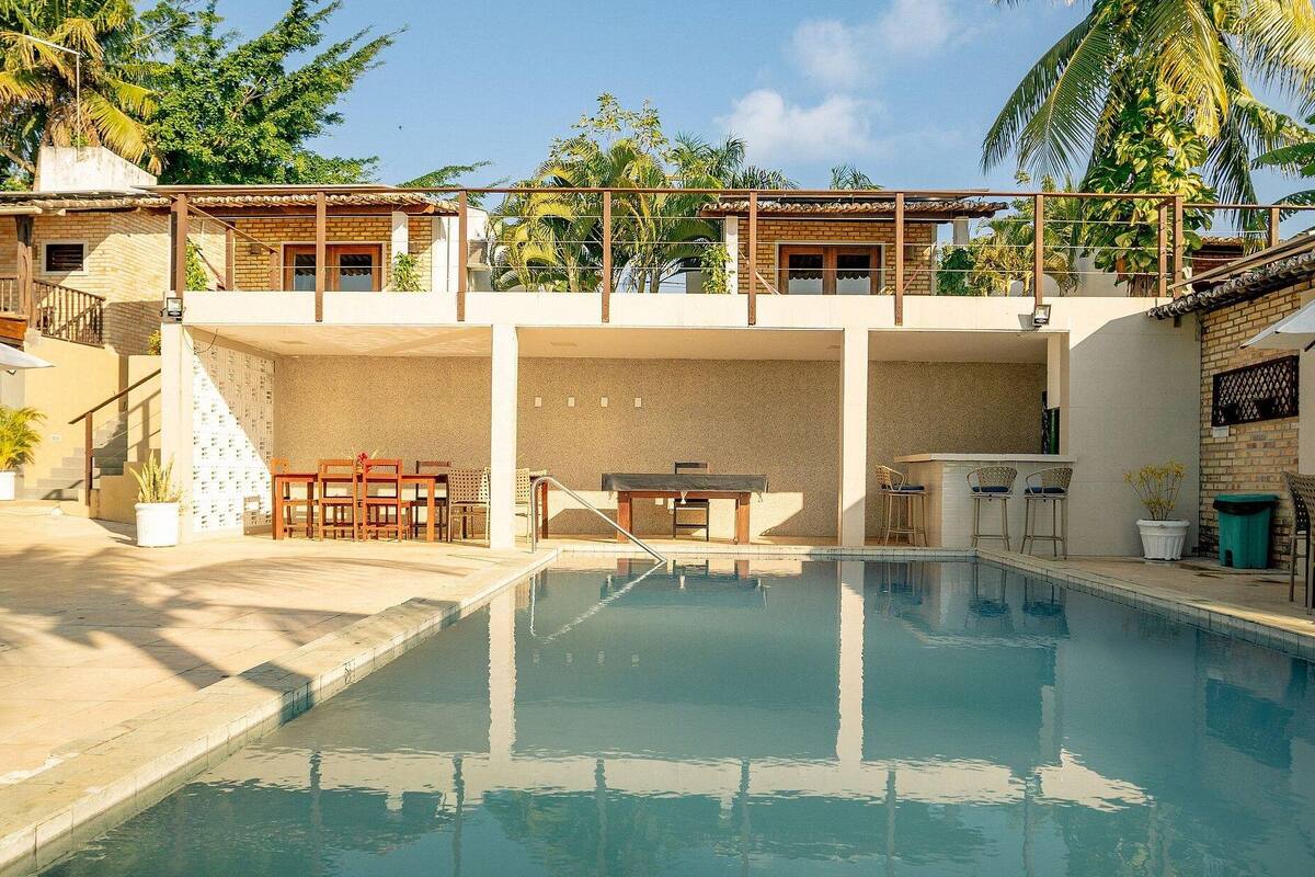 A swimming pool with a sun terrace, outdoor seating, and a view of the surrounding greenery.