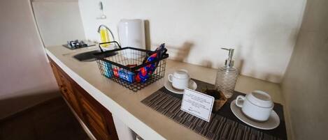 A breakfast bar with a coffee maker, a basket of condiments, and a sign indicating breakfast hours.
