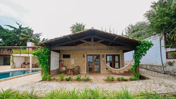 Una casa con fachada de ladrillo, un porche cubierto, una hamaca y una piscina.