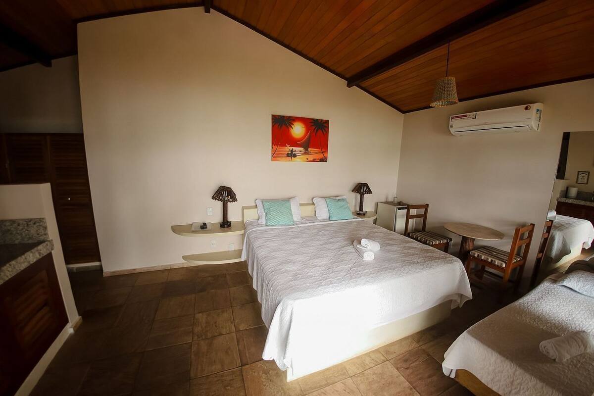 A bedroom with a bed, bedside tables, a chair, a small table, and an air conditioning unit.