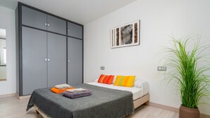 Une chambre à coucher avec un lit, une armoire grise, une plante en pot et un tableau encadré au mur.