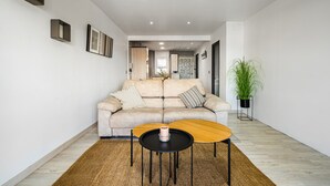 Un salon moderne avec un canapé beige, deux tables basses noires et une grande plante en pot.