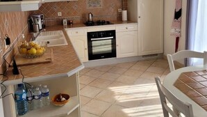 A compact kitchen with white cabinets, a tiled backsplash, a built-in oven, and a dining area with a table and chairs. - VILLA 3 STARS 10 PEOPLE SWIMMING POOL SHOPS 1.2 km BEACHES  (Saint-Georges-de-Didonne)
