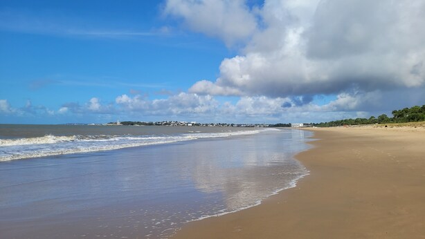 A beach with a wide sandy shore, gentle waves, and a distant view of buildings and trees under a partly cloudy sky. - VILLA 3 STARS 10 PEOPLE SWIMMING POOL SHOPS 1.2 km BEACHES  (Saint-Georges-de-Didonne)