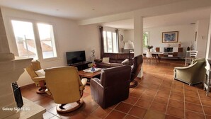 A spacious living room with a brown leather sofa, a yellow armchair, and a dining area with a table and chairs. - VILLA 3 STARS 10 PEOPLE SWIMMING POOL SHOPS 1.2 km BEACHES  (Saint-Georges-de-Didonne)