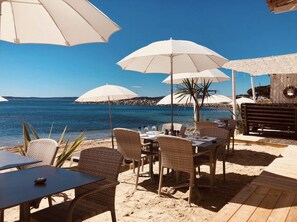 An outdoor seating area with wicker chairs and tables, white umbrellas, and a view of the sea. - Sea view apartment - Les Issambres (Roquebrune-sur-Argens)