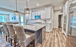 A modern kitchen with white cabinets, a marble island, wicker chairs, and stainless steel appliances. - Bayside * 5BR Fenwick Island Luxury Twin-House (Selbyville)