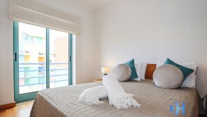 Habitación de hotel con cama, mesita de noche, lámpara y vista a un edificio a través de una puerta de vidrio.