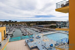 A marina with boats docked, a swimming pool with lounge chairs, and a view of the surrounding landscape. - Marina Views T2 Apartment (Albufeira)