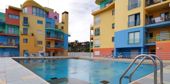 A swimming pool with a metal ladder, surrounded by colorful buildings with balconies and windows. - Marina Views T2 Apartment (Albufeira)