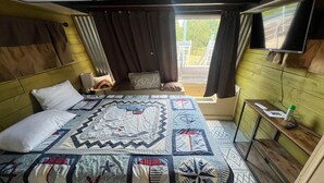 Une chambre avec un grand lit, une fenêtre avec des rideaux, un téléviseur fixé au mur et une petite table avec une télécommande.