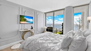 Quarto com uma cama grande, televisão na parede e varanda com vista para o mar.