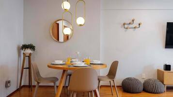 A dining area with a round table, four chairs, a mirror, pendant lights, and a television on the wall.
