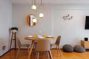 A dining area with a round table, four chairs, a mirror, pendant lights, and a television on the wall.