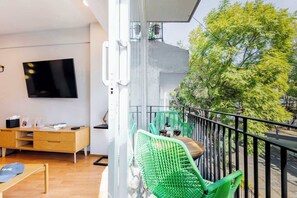 Un balcon avec des chaises vertes, une table en bois et un téléviseur fixé au mur.
