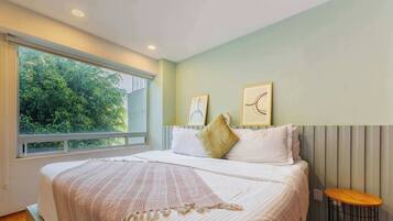 A bedroom with a large bed, a bedside table, and a window with a view of trees.