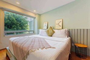 A bedroom with a large bed, a bedside table, and a window with a view of trees.