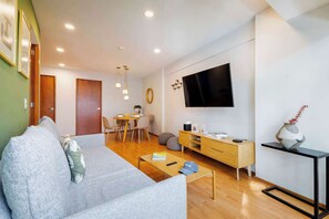 A modern living room with a sofa, coffee table, TV, and a dining area with chairs and a table.