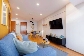 A modern living room with a sofa, a dining table, and a TV mounted on the wall.