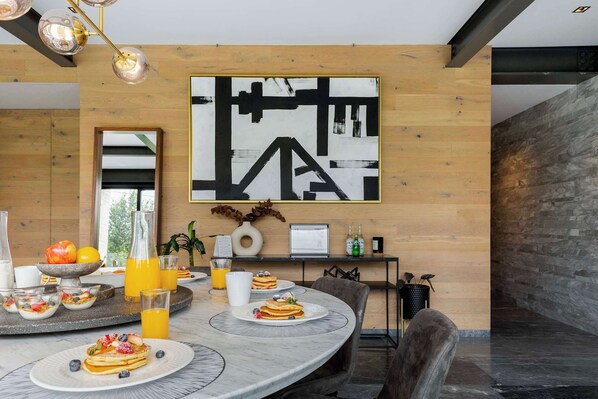 A modern dining area with a round table, breakfast setup, and a large abstract painting on the wall.