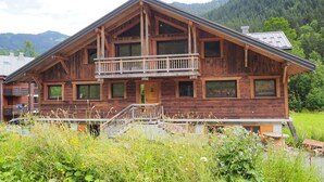 Un chalet in legno con un balcone, immerso nel verde e con le montagne sullo sfondo.