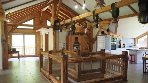 Una stanza spaziosa con soffitto alto, travi in legno, un grande tavolo di legno e un angolo cottura con elettrodomestici moderni.