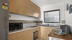 A modern kitchen with wooden cabinets, a stainless steel microwave, a built-in oven, a sink, and a window above the sink.
