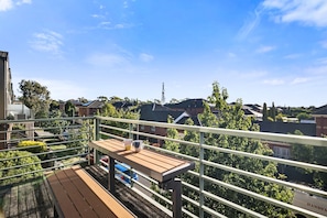 Ein Balkon mit Holztisch und Stühlen, mit Blick auf eine Wohngegend mit Häusern und Bäumen.
