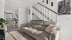 A modern living room with a grey sofa, a staircase, and a kitchen in the background.