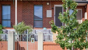 A two-story residential building with a balcony on the upper floor, a brick facade, and a metal gate in front.