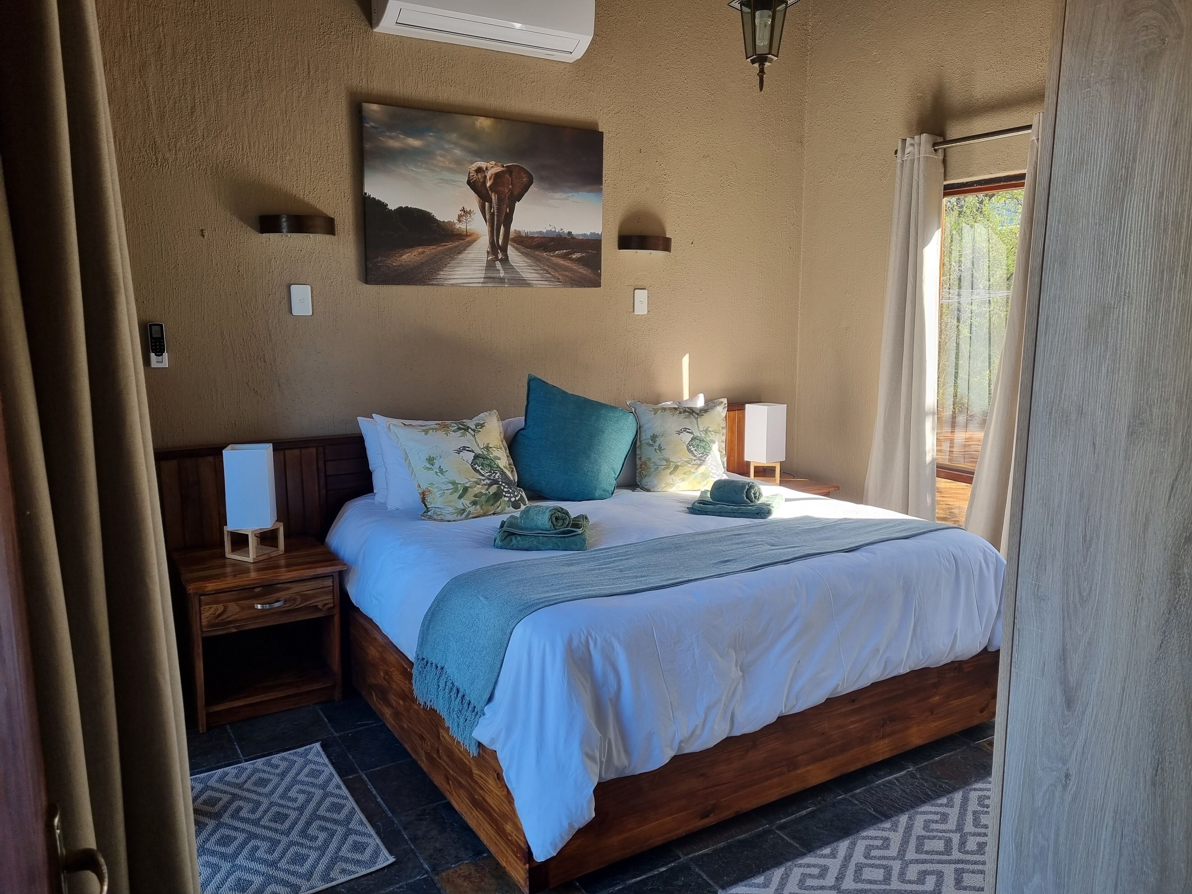 Un dormitorio con cama de madera, mesita de noche, lámpara de pared, un cuadro y una ventana con cortinas.